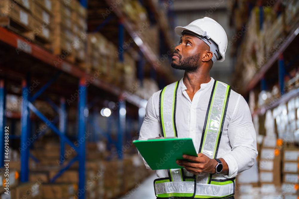 Portrait of an African warehouse manager holding a clipboard checking inventory in a large distribution center. Portrait of an African warehouse manager holding a clipboard checking inventory in a large distribution center.