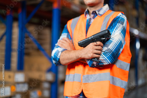 Closeup warehouse worker standing in large warehouse distribution center holding barcode reader.