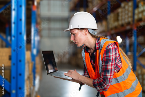 Warehouse worker working process checking the package using laptop in large warehouse distribution center. Caucasian female inspects storage and inventory.