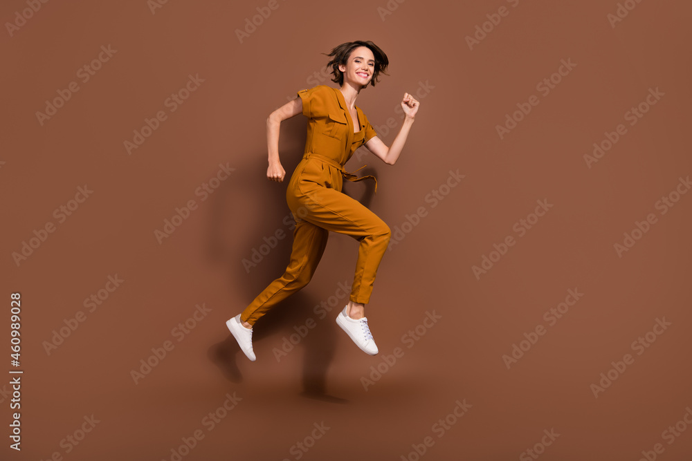 Full length photo of cheerful joyful happy young woman jump up run sale season isolated on brown color background Full length photo of cheerful joyful happy young woman jump up run sale season isolated on brown color background