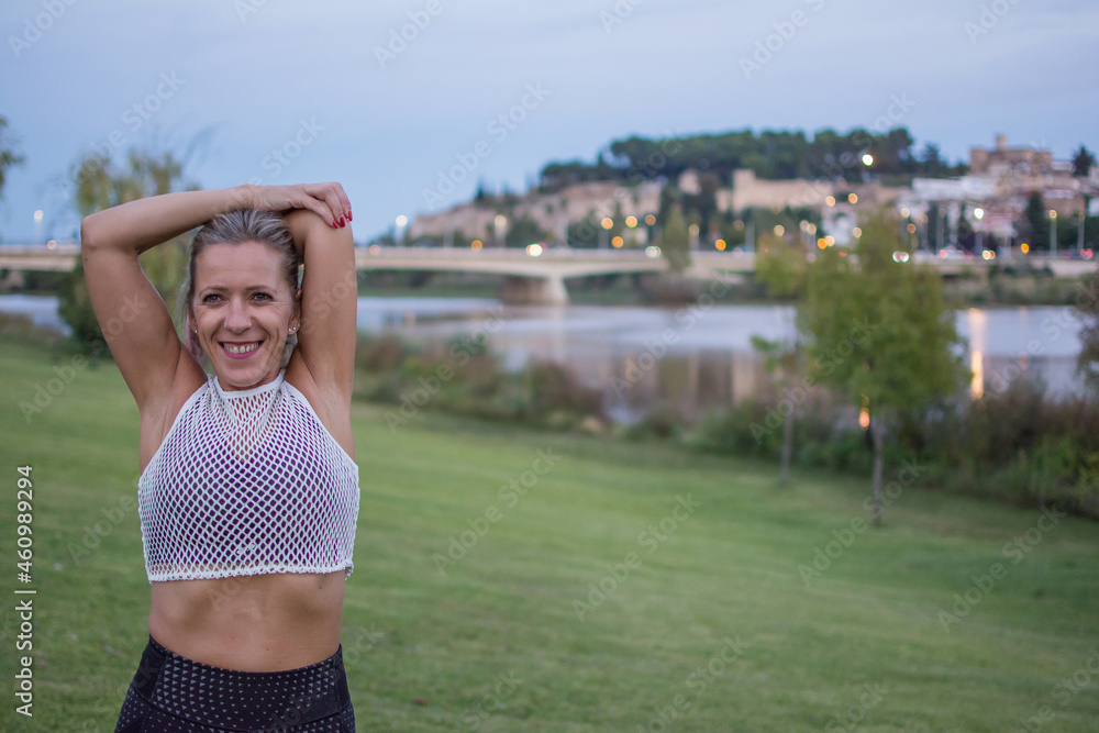 Portrait Of Sporty  Woman Stretching Arms.
Portrait Of sporty  Woman Looking Away With The City At The Background. She Is Concentrated While Stretching Arms.