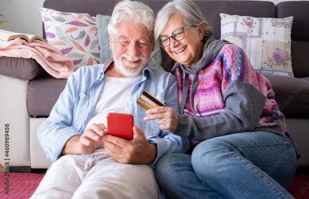 Happy senior couple in living room at home having fun shopping online paying with credit card, e-commerce, buyer, consumerism concept Happy senior couple in living room at home having fun shopping online paying with credit card, e-commerce, buyer, consumerism concept