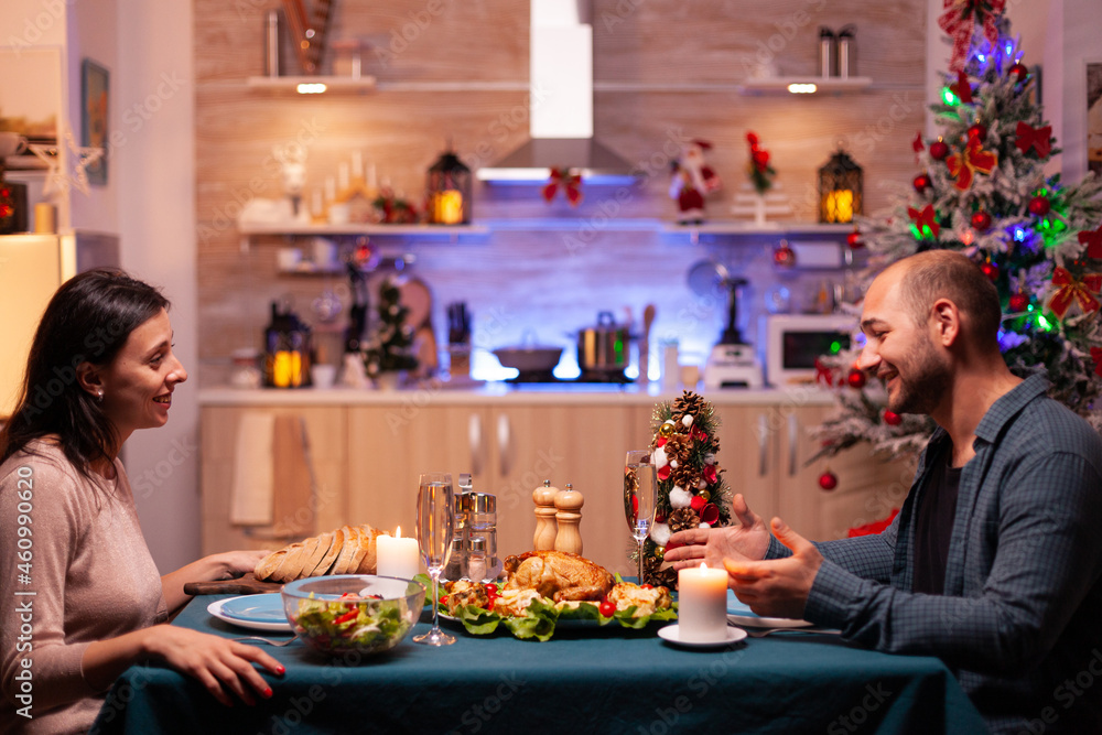 Happy family sitting at romantic dining table in xmas decorated kitchen enjoying christmas dinner together. Cheerful people enjoying winter holiday season celebrating christmastime - obrazy, fototapety, plakaty 