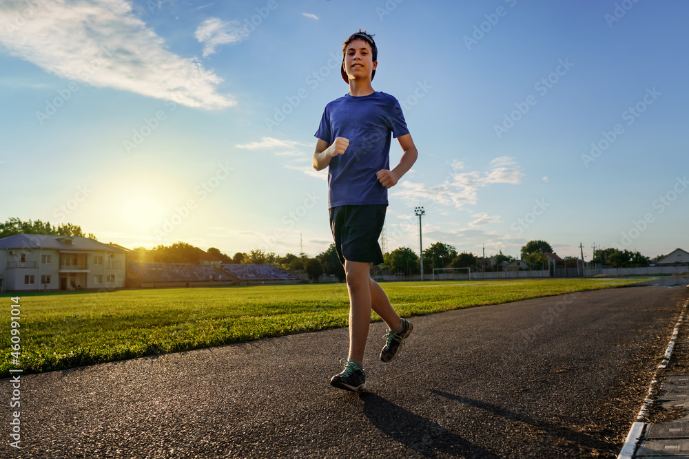 concept of sports and health - teen boy runs along the stadium track, a soccer field with green grass. concept of sports and health - teen boy runs along the stadium track, a soccer field with green grass.