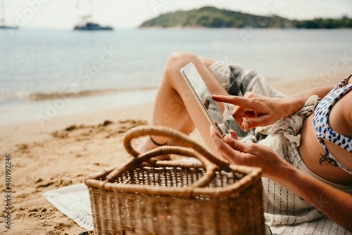 Caucasian female relaxing on beach reading book off digital tablet