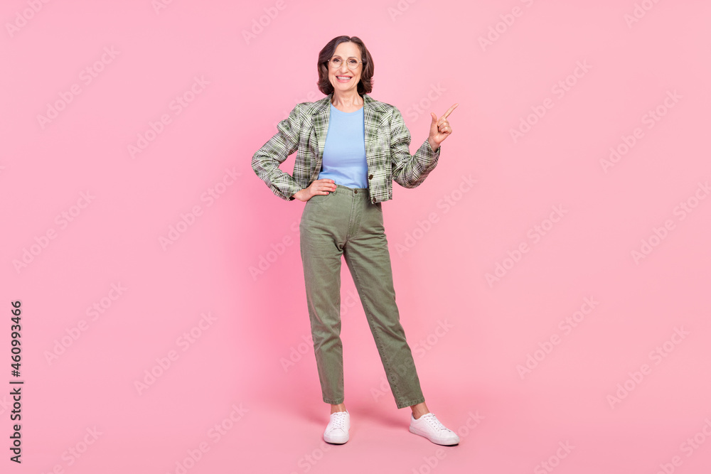 Full length photo of cheerful old woman point finger empty space news garage sale clothes isolated on pastel pink color background Full length photo of cheerful old woman point finger empty space news garage sale clothes isolated on pastel pink color background