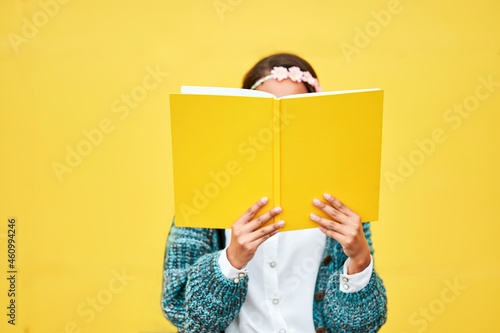 Young woman reading yellow book by wall photo