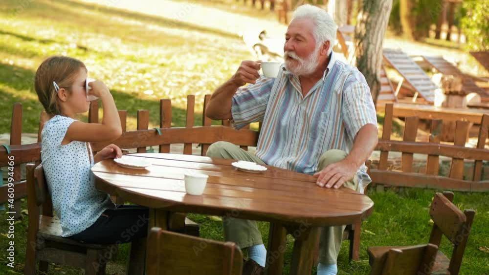 Grandfather and little girl playing to drink coffee sitting on a small children's wooden table in the yard Grandfather and little girl playing to drink coffee sitting on a small children's wooden table in the yard