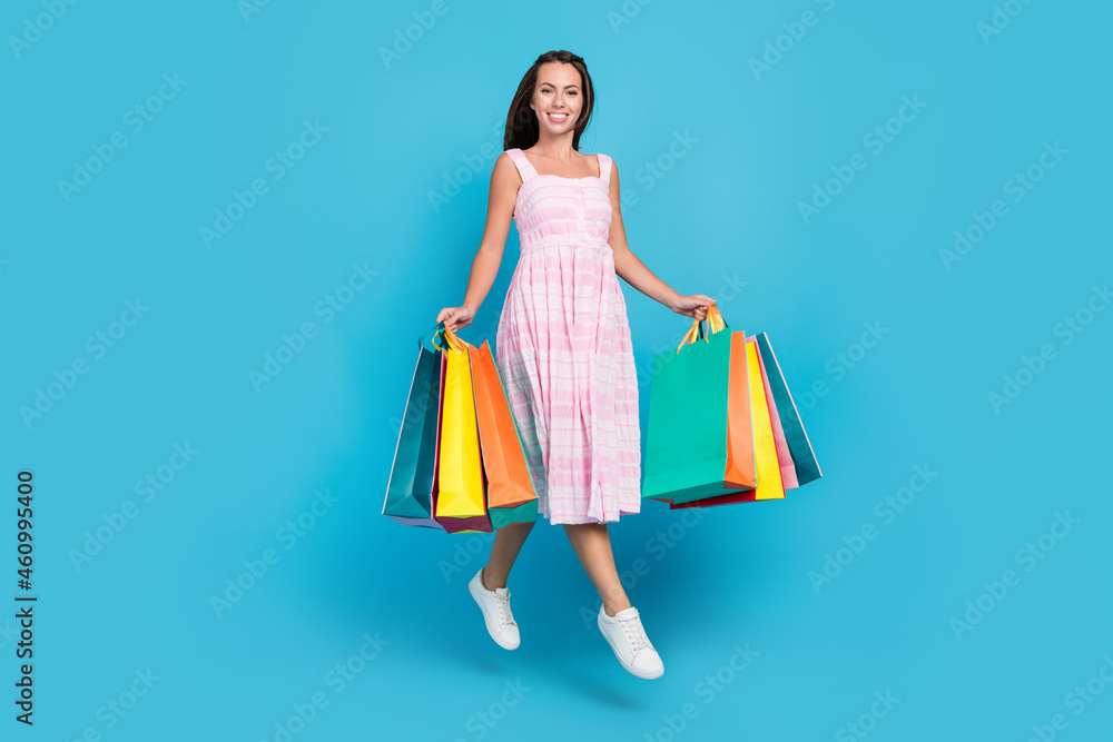 Full length photo of brunette haired stylish attractive beautiful woman jump hold shop bags sale isolated on blue color background