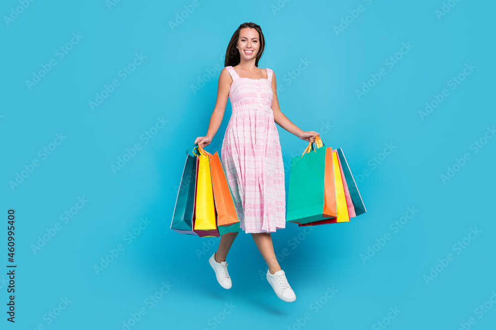 Full length photo of brunette haired stylish attractive beautiful woman jump hold shop bags sale isolated on blue color background Full length photo of brunette haired stylish attractive beautiful woman jump hold shop bags sale isolated on blue color background