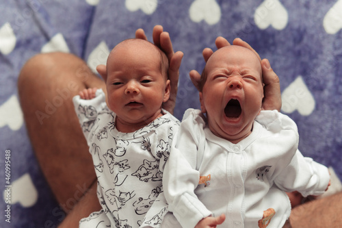 Close-up portrait of newborn twins laying by heads in father's hands. Yawning newborn girl. Cute and tender photo of newborn twin girls. Selective focus. Film grain photo