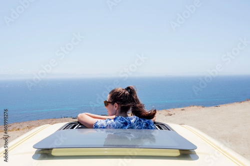 Mid adult woman wearing sunglasses leaning through sunroof of van during summer photo