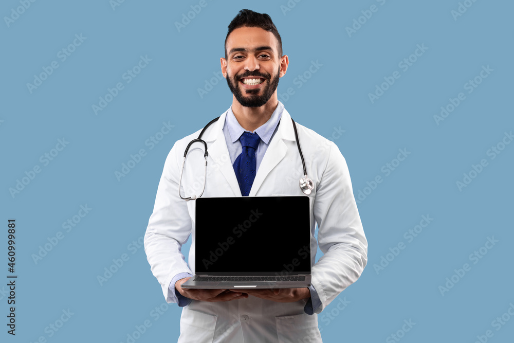 Arabic Male Doctor Showing Laptop Empty Screen Over Blue Background Arabic Male Doctor Showing Laptop Empty Screen Over Blue Background