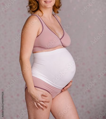 Pregnant woman's belly in special underwear. Medical bandage to support the abdomen. Healthy pregnancy. Pink pajamas cotton. Corset for carrying. Third trimester. 