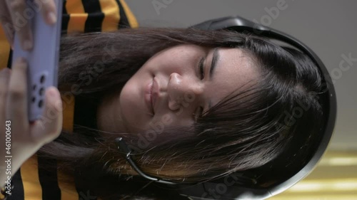 Vertical portrait Asian chubby cute teen girl enjoy playing online games and chatting to friends with headset on smartphone at home. Close up happy plump female teenager lifestyle.