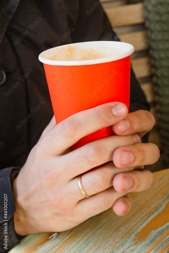 Red paper cup with hot tea or coffee in a man's hand in a cafe. Vertical photo Red paper cup with hot tea or coffee in a man's hand in a cafe. Vertical photo
