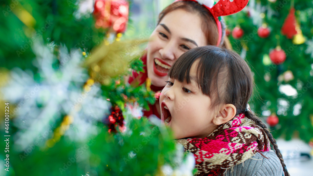 Attractive Asian mother and daughter wearing winter outfits and decorating Christmas tree at home with joy, preparing to celebrate Christmas festival. Concept for family Christmas party