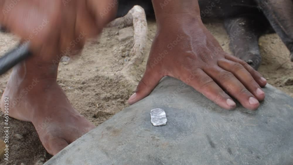 LATIN MAN HANDS molding LEAD in sheets CRAFTLY WITH hammer on a large stone and with bare feet