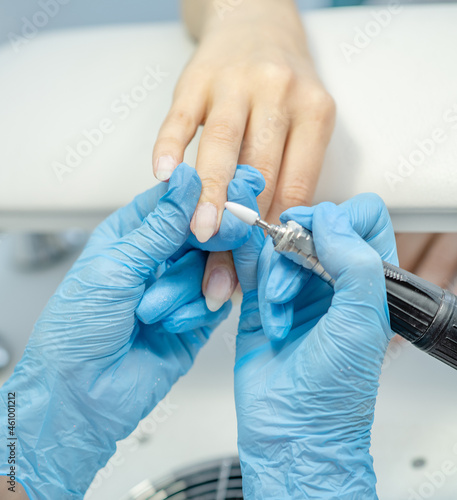 Professional manicure master using electric machine in beauty salon to remove nail polish hands during manicure procedure