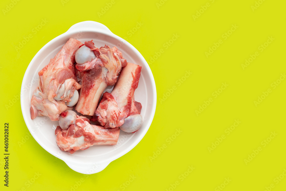Raw pork bones in white plate on green background.