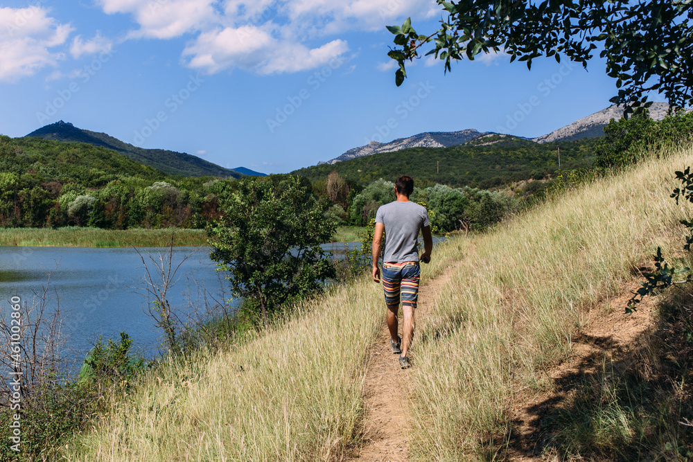 A young man is walking alone by the lake with a mountain landscape A young man is walking alone by the lake with a mountain landscape