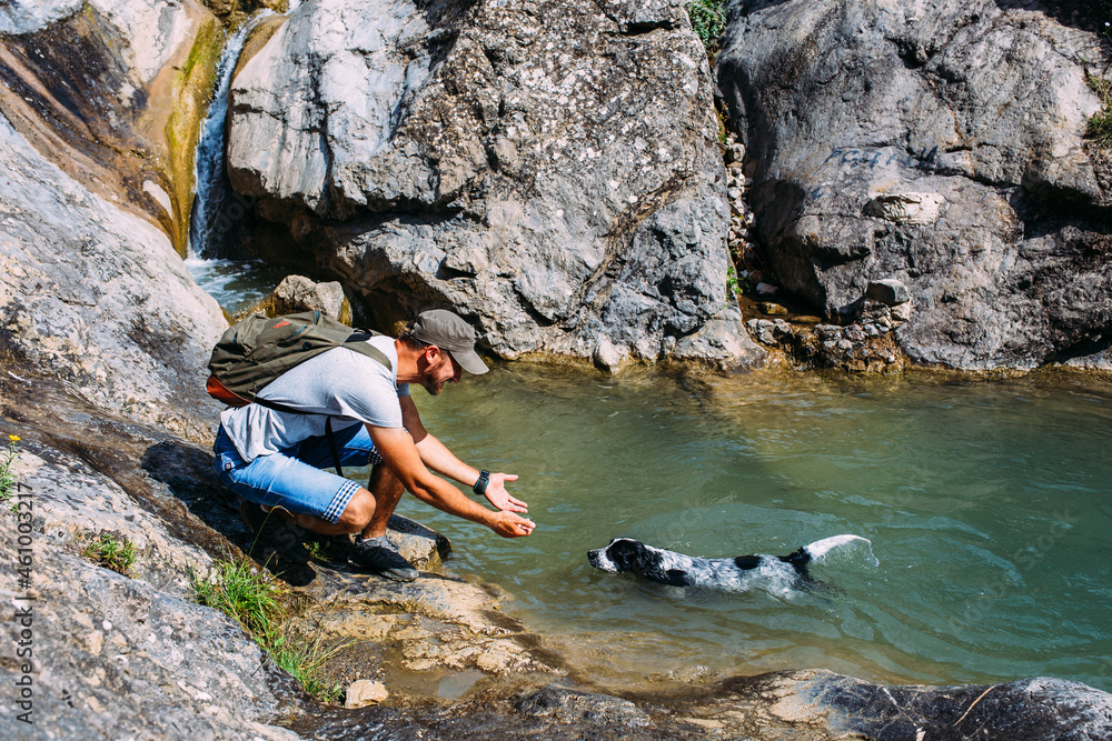 Male owner of spaniel dog walking against mountains and waterfall background.