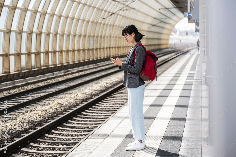 Teenage girl with backpack using mobile phone at train station Teenage girl with backpack using mobile phone at train station