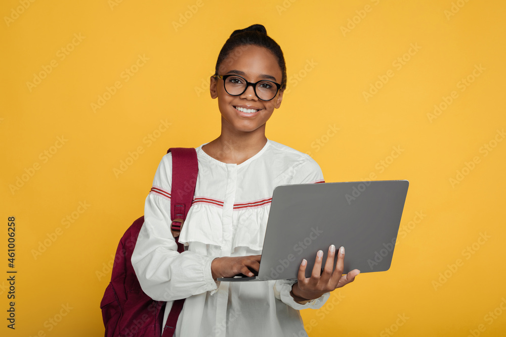 Smiling smart cute teenage african american girl pupil in glasses with backpack studying with laptop