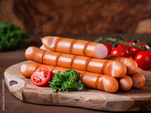Styled Grilled Frankfurter sausages on wooden board with tomatoes and green herbs