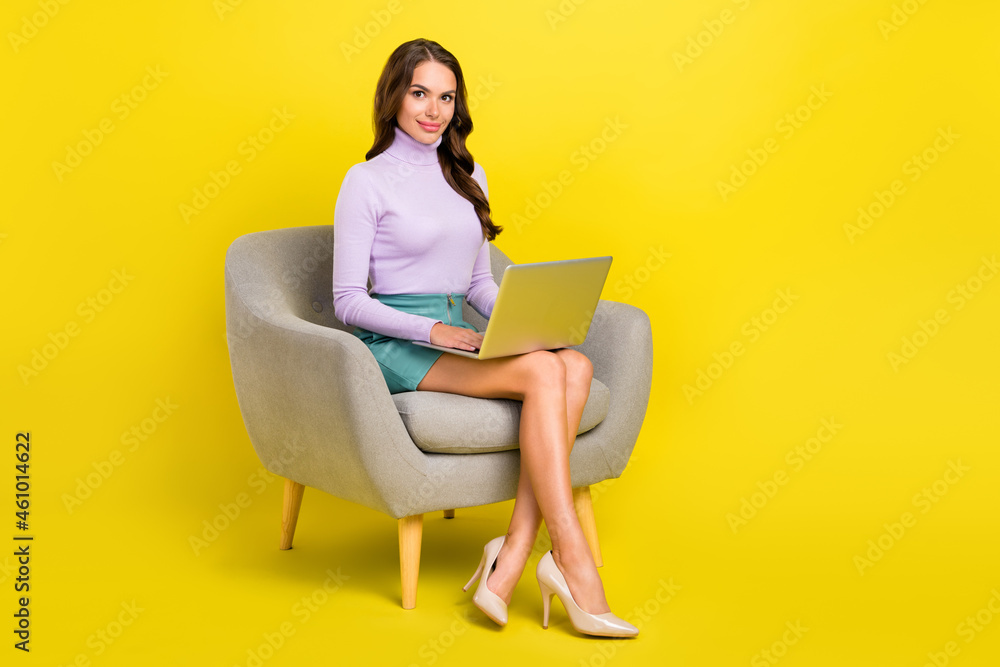 Full size photo of pretty charming person sit on chair use netbook look camera isolated on yellow color background Full size photo of pretty charming person sit on chair use netbook look camera isolated on yellow color background