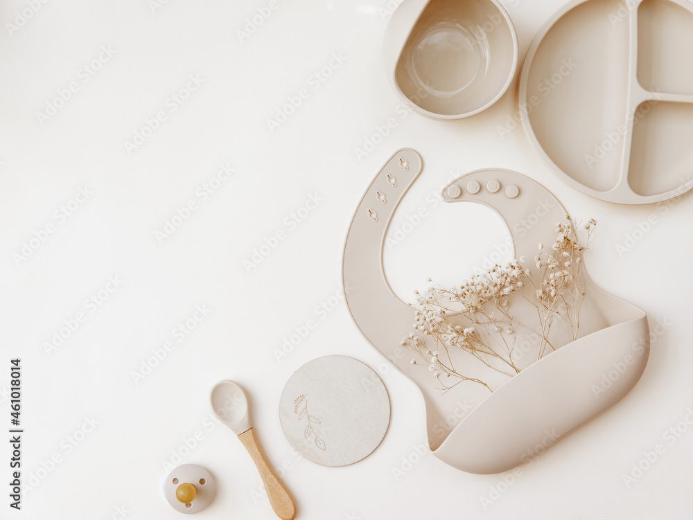 Fototapeta premium Silicone baby beige bib with spoon on neutral background. Top view, flat lay