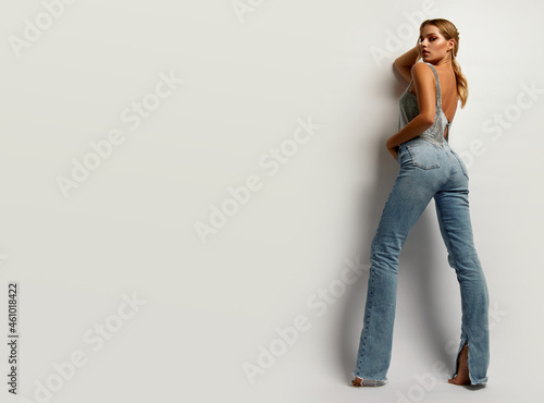 Young tanned woman in jeans and shiny top in the studio on a white background.Model posing in the studio.Advertising fashion clothes.Advertising concept.