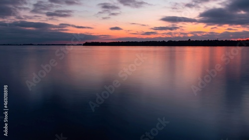 Sunset on a cloudy sky over a water surface with an island on the horizon. River landscape
