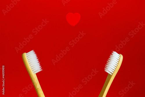 Two bamboo toothbrushes on a red background. above them a symbol of love heart.