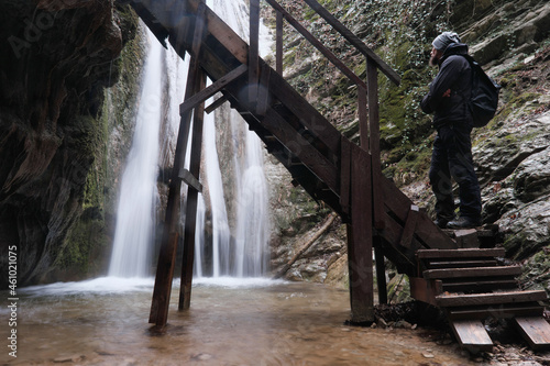 A hiker (man) looking at The Devil's Mouth waterfall in Teshebs river gorge on winter day. Gebiusskie waterfalls, Krasnodar Krai, Caucasus, Russia. photo