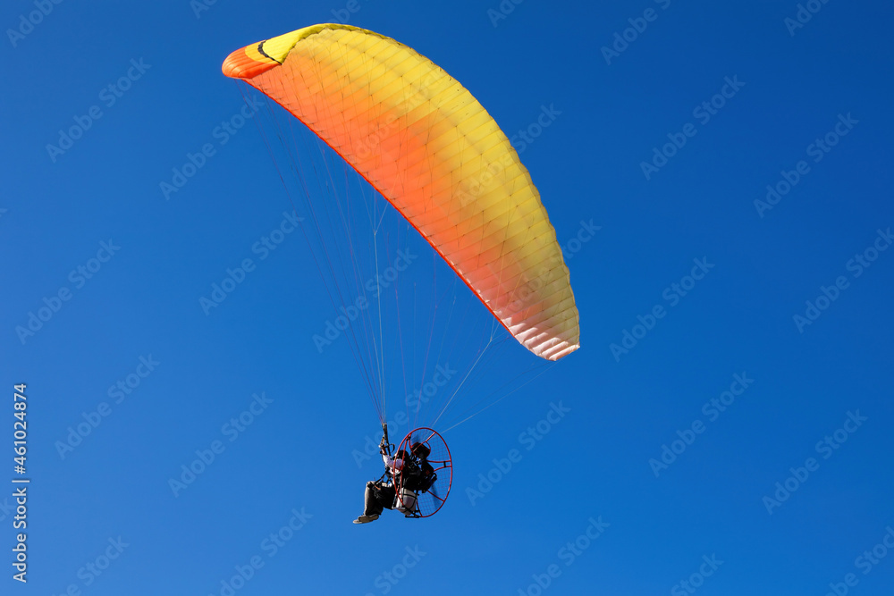 Yellow Powered Parachute, operated by pilot flies flies in the bright blue sky Yellow Powered Parachute, operated by pilot flies flies in the bright blue sky