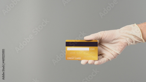 Hand is wear white medical glove and showing back of gold credit card isolated on grey background.