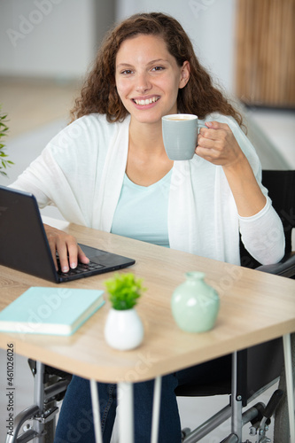 cheerful disabled woman using her laptop while drinking coffee