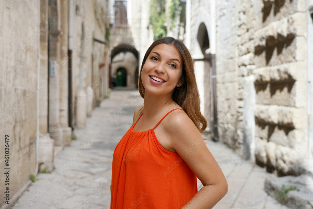 Close up outdoor portrait of beautiful woman in orange dress turn around while walking in historic medieval town Close up outdoor portrait of beautiful woman in orange dress turn around while walking in historic medieval town