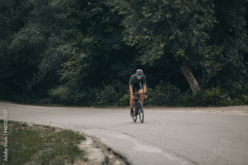 Athletic man in sport clothes cycling among green forest