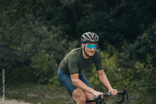 Positive man in activewear cycling among green forest