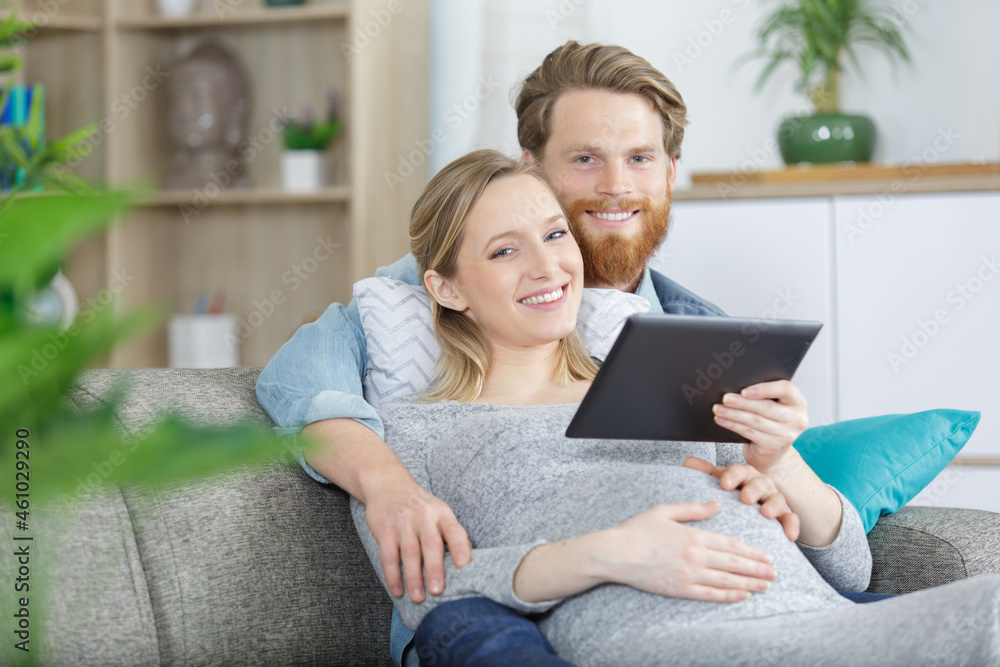 young happy couple with digital tablet hugging on sofa