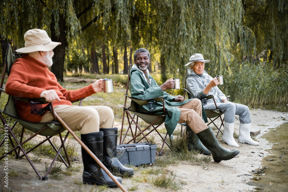 Smiling multicultural senior men in fishing outfit with thermo