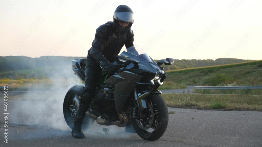 Biker performing tire burnout with lots of smoke. Motorcycle wheel are slip on route during start of movement. Wheel of sport motorbike starting to spin at asphalt road. Slow motion Close up Side view Biker performing tire burnout with lots of smoke. Motorcycle wheel are slip on route during start of movement. Wheel of sport motorbike starting to spin at asphalt road. Slow motion Close up Side view