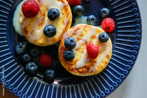 Delicious hot cheesecake served with fresh blueberries and raspberries and poured with condensed milk. Healthy tasty breakfast on a blue plate