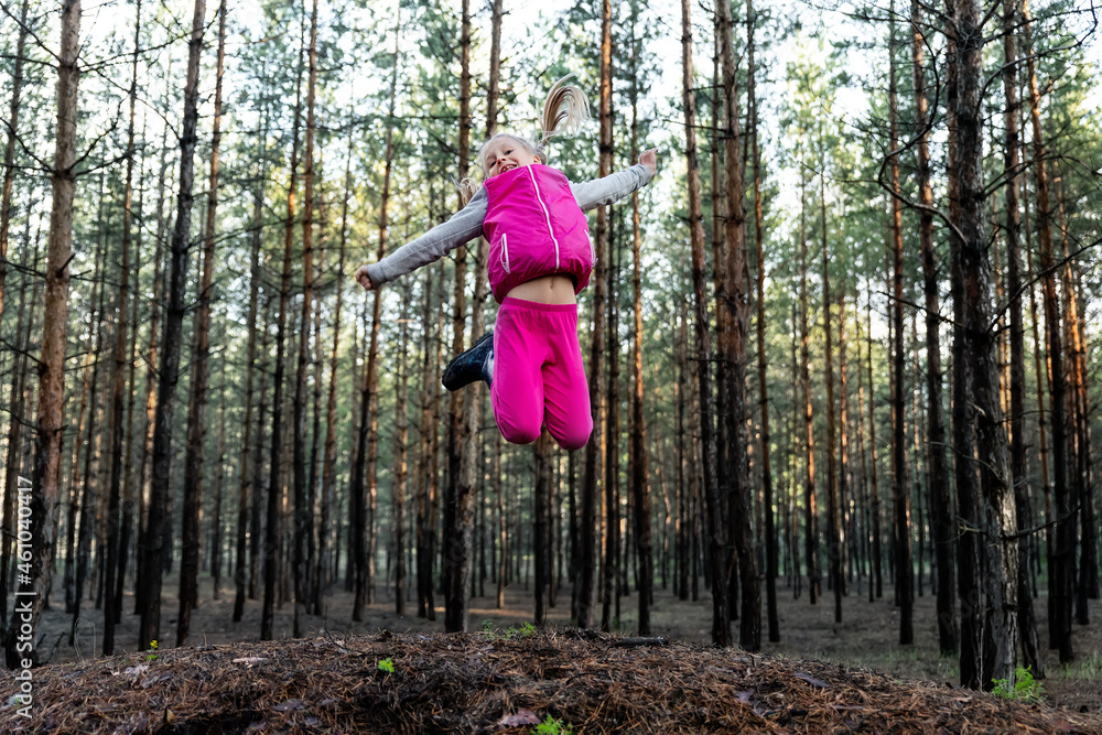 Cute pretty blond caucasian happy child funny girl in bright pink suit enjoy walking in wet coniferous pine forest on sunny morning day. Little female kid portrait hiking nature trip outdoors Cute pretty blond caucasian happy child funny girl in bright pink suit enjoy walking in wet coniferous pine forest on sunny morning day. Little female kid portrait hiking nature trip outdoors