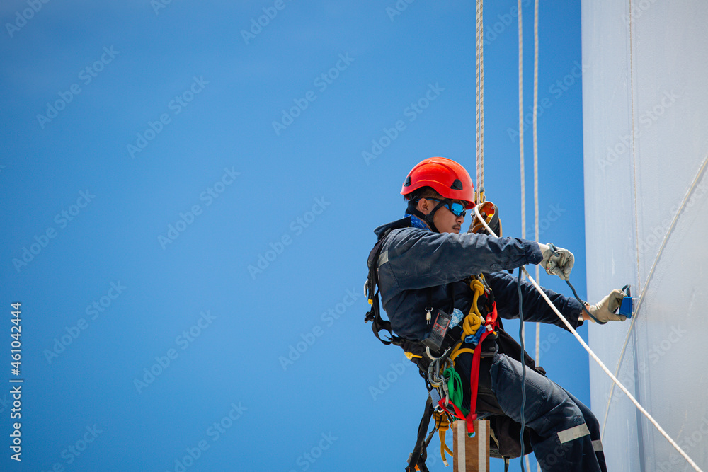 Closeup male workers control swing rope down height tank rope inspection tank gas background blue sky. - obrazy, fototapety, plakaty 