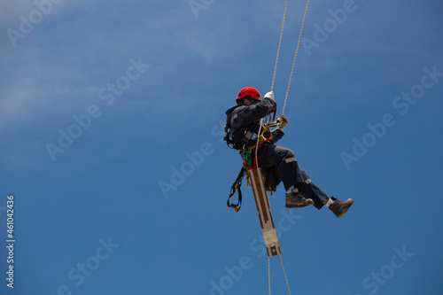 Male workers control swing rope down height tank rope access inspection of thickness tank gas background blue sky.