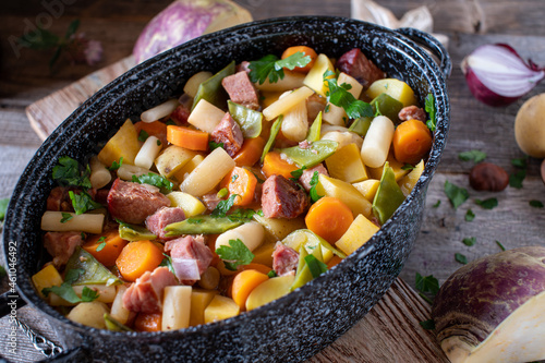 Stew with root vegetable, meat and potatoes in a rustic pot on wooden table  photo