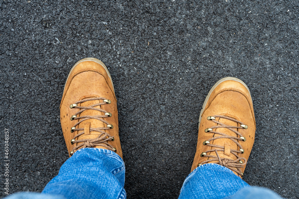 The technician's legs, wearing blue jeans and brown leather shoes, stand on a black paved road